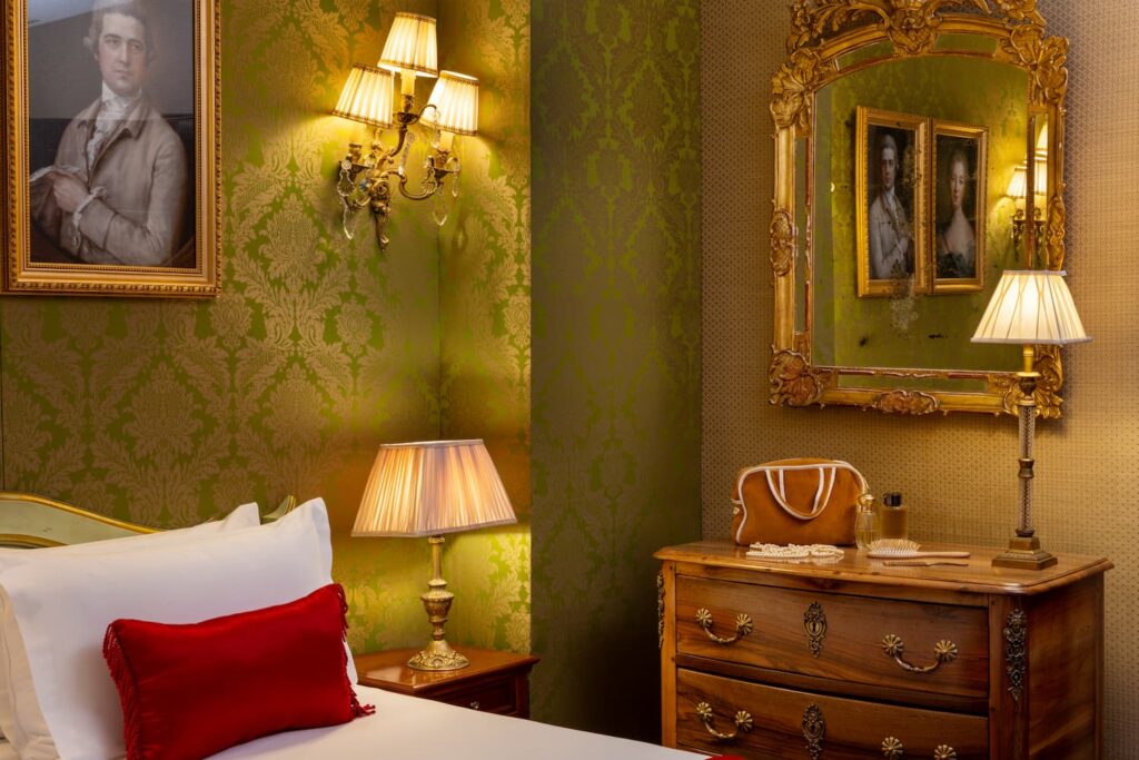 Habitación de hotel con telas verdes, cómoda de madera, espejo y lámparas encendidas | Habitación romántica en París | Hotel de Seine París
