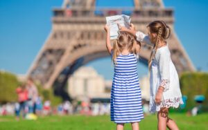 two young girls looking at a city map facing the Eiffel Tower on a sunny day | visit Paris with kids
