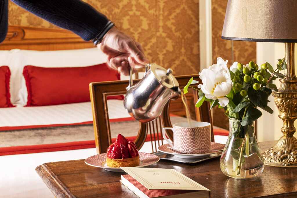 Hotel room, with a hand serving a coffee, a strawberry pie and flowers - Hotel in Paris with concierge service