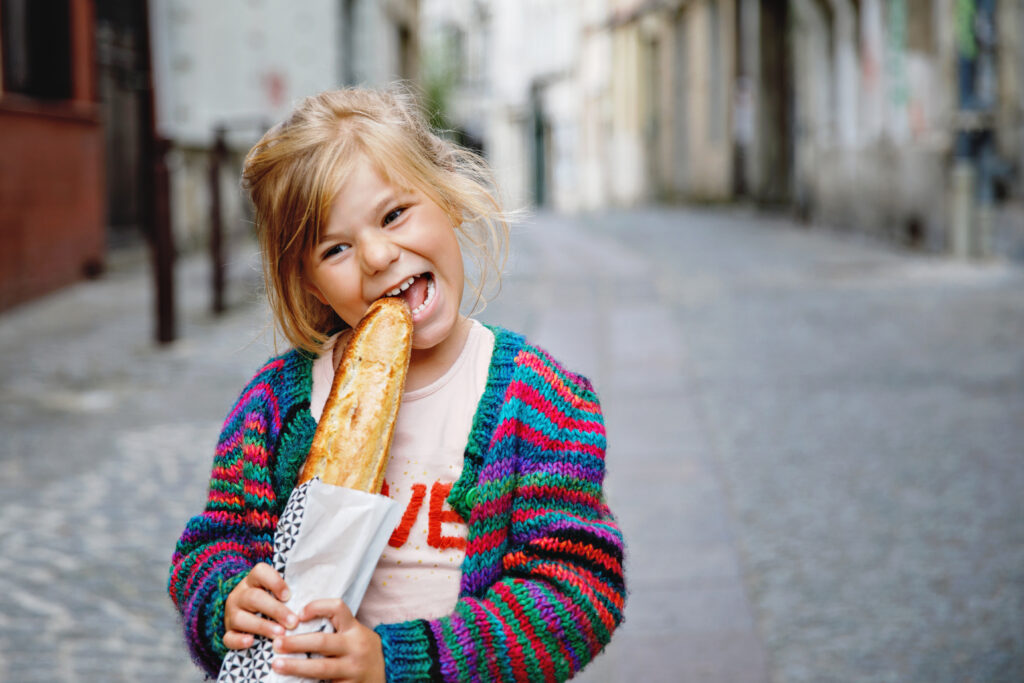 young girl eating a French baguette in a Parisian street | visit Paris with kids